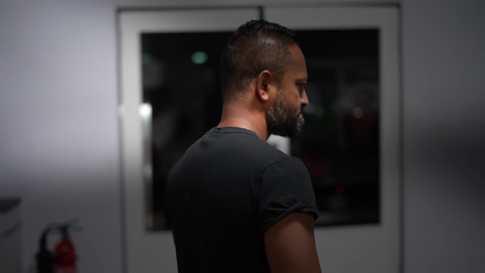 A bearded man in a black T-shirt, seen from behind